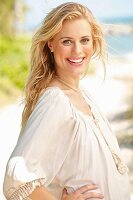 A young blonde woman on a beach wearing a white blouse