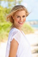 A young blonde woman on a beach wearing a white lace blouse