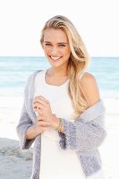 Young blonde woman wearing white dress and lilac cardigan on beach