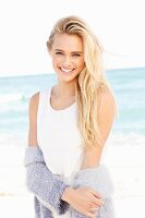 Junge blonde Frau in weißem Kleid und lila Strickjacke am Strand