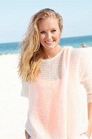 A blonde woman on the beach wearing a see-through woollen jumper