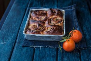 Apple and cinnamon buns in a baking dish next to mandarins