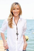 A young blonde woman by the sea wearing a white blouse and jeans