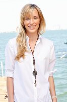 A young blonde woman by the sea wearing a white blouse and jeans