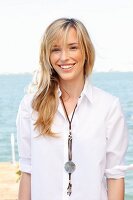 A young blonde woman by the sea wearing a white blouse and jeans