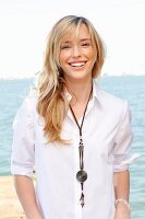 A blonde woman by the sea wearing a white shirt and jeans