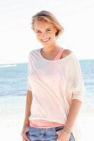 A blonde woman by the sea wearing two tops and jeans