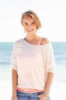 A blonde woman by the sea wearing two tops and jeans