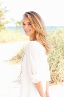 A young blonde woman on a beach wearing a white tunic