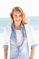 A young woman on a beach wearing a denim shirt and a cardigan