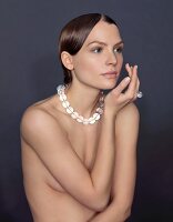 A topless brunette woman wearing a necklace and a ring made of glass beads