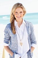 Junge Frau in weisser Bluse und Strickjacke am Strand