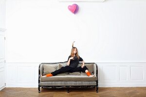 Junge Frau sitzt mit gegrätschten Beinen auf altem Sofa