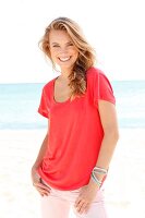 A blonde woman on a beach wearing a red top and pink trousers