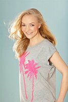 A young blonde woman wearing a grey sequinned T-shirt with palm trees