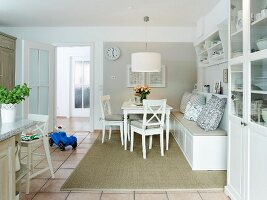 weiße Wohnküche im Landhausstil mit gemütlicher Sitzbank, Vitrinenschrank und Fliesenboden