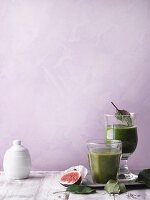Two green smoothies garnished with figs and leaves