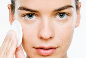 A young woman cleaning her face with a cotton pad