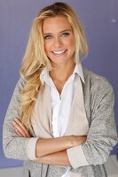 A young blonde woman wearing a white blouse and a grey shirt jacket