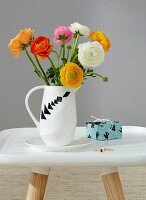 A bunch of buttercups in a white jug decorated with various tangram shapes next to a small present