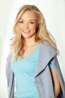 Junge blonde Frau in hellblauem Top und grauem Pulli um Schultern