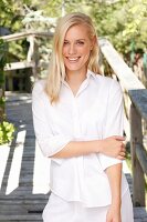 A young blonde woman on a wooden jetty wearing a white blouse