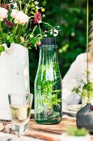 Mineralwasser mit frischen Kräutern in Glaskaraffe auf Gartentisch