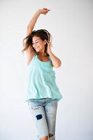 A young woman wearing torn jeans and a turquoise top dancing