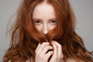 Portrait einer jungen Frau, die mit ihren roten Haaren spielt