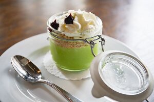 A creamy green dessert with biscuit crumbs, blackberry purée and whipped cream in a glass
