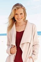 A young blonde woman on a beach wearing a bordeaux red top and a light fleece