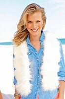 A young blonde woman on a beach wearing a light denim blouse and a fur scarf