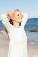 A young blonde woman on a beach wearing a pastel green jumper