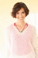 Brünette Frau in rosa Top und transparentem weissen Strickpulli