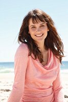A brunette woman in a pink long-sleeved top on the beach