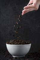 A hand throwing coffee beans into a bowl