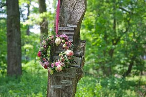 Wreath of flowers hung on board with small signs in woodland