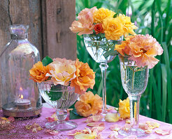 Blüten von Rosa (Rosen, gelb und orange) in Gläsern auf dem Tisch