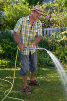 Man watering lawn with hose and sprinkler