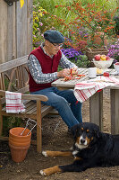 Großvater sitzt mit Hund am Tisch und schält Malus (Äpfel)