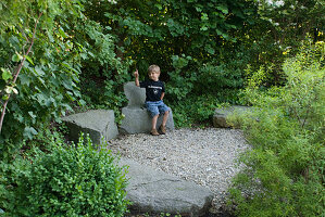 Kleiner Kiesplatz mit Granit - Blöcken , Junge sitzt auf Stein-Sessel