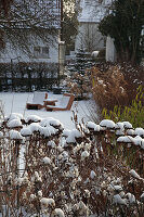 Verschneiter Garten am Haus mit Fruchtständen von Sedum (Fetthenne) und anderen Stauden, wetterfeste Sitzgruppe, Hecke, Picea (Stechfichte)