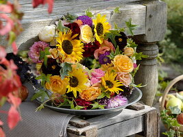 Kranz aus Sonnenblumen ,Rosen und Dahlien auf Weinkiste angelehnt an Bank