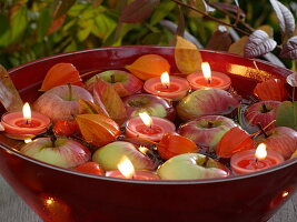 Rote Schwimmschale mit Äpfeln und Kerzen