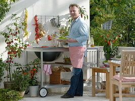 Outdoor-Küche auf dem Balkon: Mann grillt Paprika, Töpfe mit Glockenchili