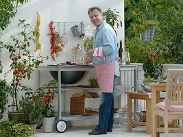 Outdoor-Küche auf dem Balkon: Mann grillt Aubergine, Töpfe mit Glockenchili