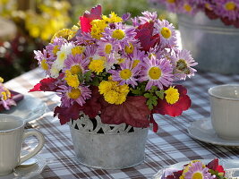 Herbstliche Tischdeko mit Herbstchrysanthemen und Heuchera-Blättern