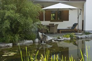 Blick vom Teich auf die Terrasse mit Korb-Möbeln