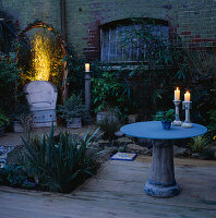 Nächtlich beleuchtete Gartenecke mit Keramikstuhl und Glaskeramiktisch mit Kerzen