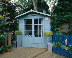 Die Terrasse 'Upper Deck' mit blauem Gartenhaus, Terrassendielen und blauem Zierzaun